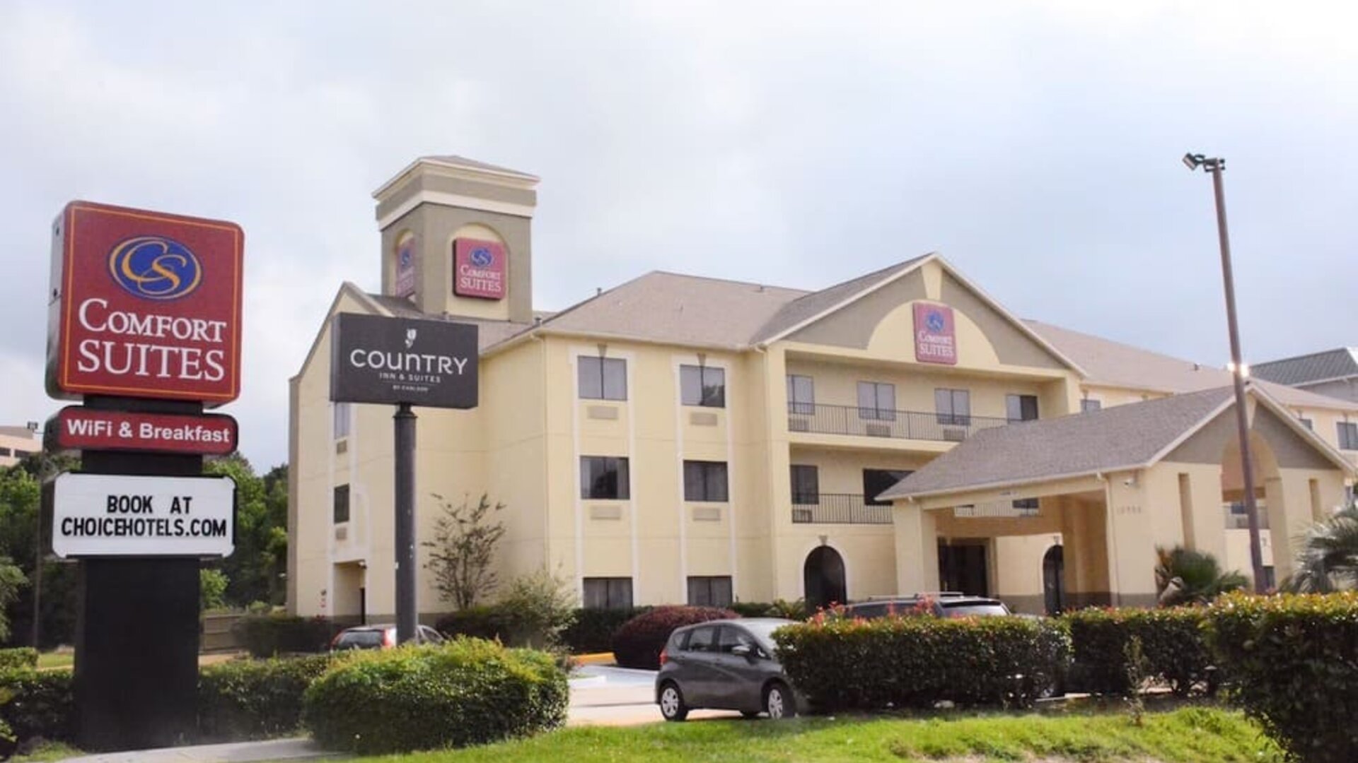 Roadside view with hotel building and branded sign near landscaped greenery at Comfort Suites Bush Intercontinental Airport.