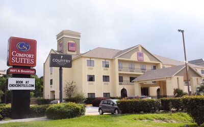 Roadside view with hotel building and branded sign near landscaped greenery at Comfort Suites Bush Intercontinental Airport.