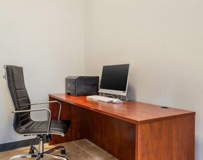 Business center desk with computer, printer, and office chair against a plain wall at Comfort Suites Bush Intercontinental Airport.