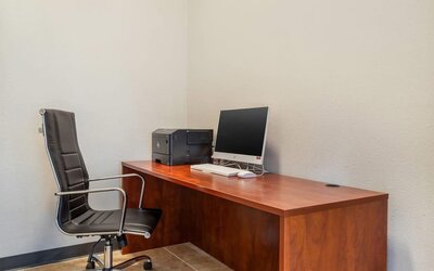 Business center desk with computer, printer, and office chair against a plain wall at Comfort Suites Bush Intercontinental Airport.