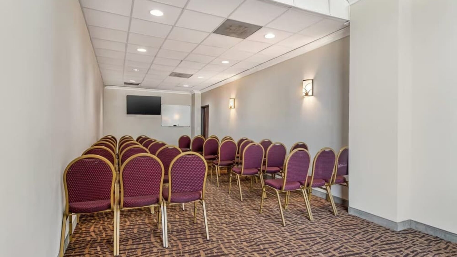 Meeting room with rows of chairs, wall-mounted TV, and whiteboard in a compact space at Comfort Suites Bush Intercontinental Airport.