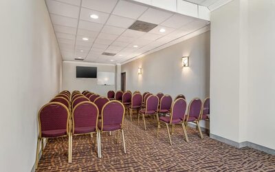 Meeting room with rows of chairs, wall-mounted TV, and whiteboard in a compact space at Comfort Suites Bush Intercontinental Airport.