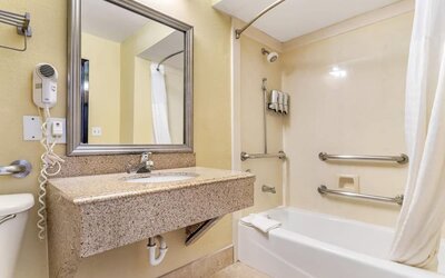 Bathroom with bathtub shower combo, grab bars, sink vanity, and wall-mounted hair dryer at Comfort Suites Bush Intercontinental Airport.