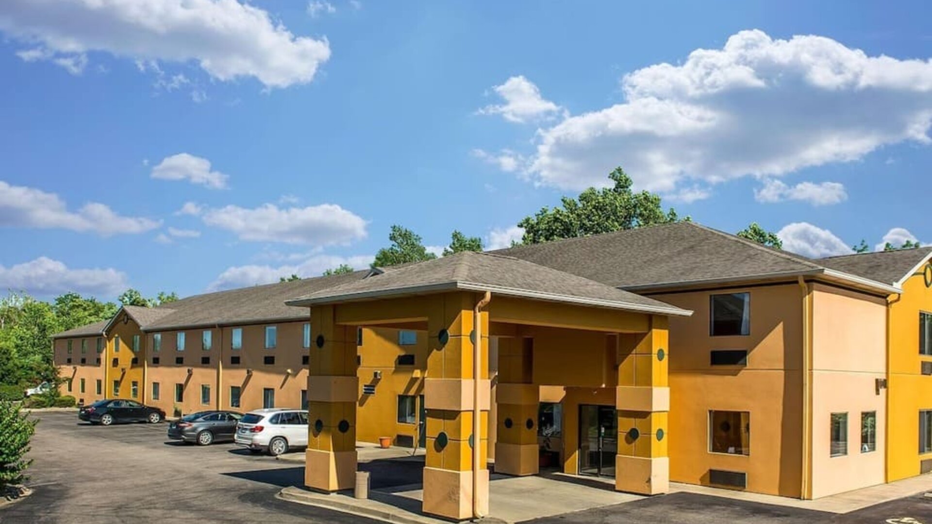 Exterior view of hotel building with covered entrance, parking area, and surrounding greenery at Suburban Studios Mason Hwy-42.
