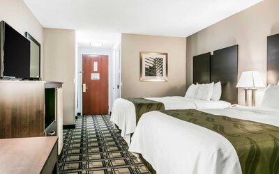 Double room with two beds, bedside table, lamp, and patterned carpet leading to entry door at Suburban Studios Mason Hwy-42.