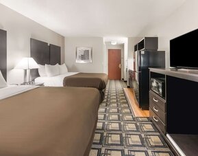 Room with two beds, dresser, TV, microwave, mini fridge, and patterned flooring at Suburban Studios Mason Hwy-42.