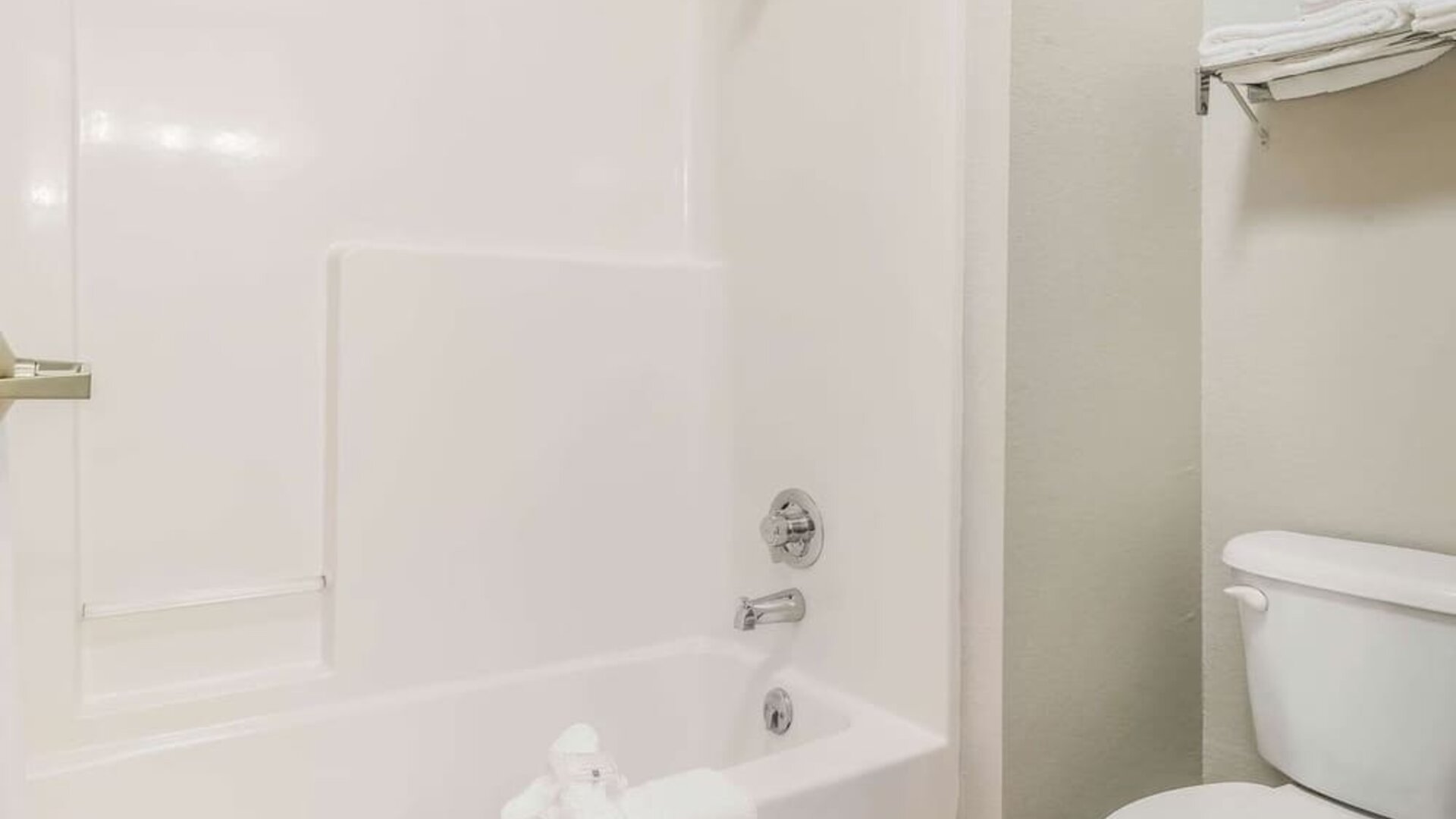 Bathroom with bathtub shower combo, toilet, and folded towels on rack at Suburban Studios Mason Hwy-42.