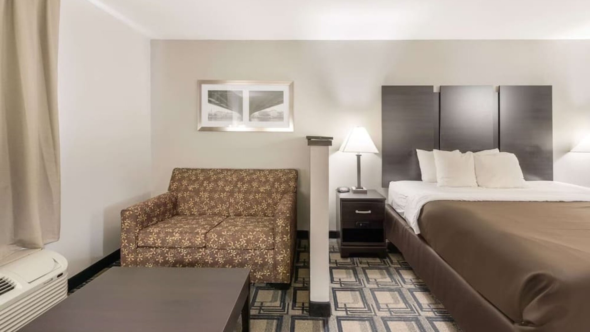 King room with sofa seating, coffee table, bedside lamps, and window with curtains at Suburban Studios Mason Hwy-42.