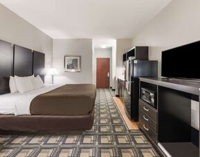 King room with desk area, TV, dresser, and patterned carpet flooring at Suburban Studios Mason Hwy-42.