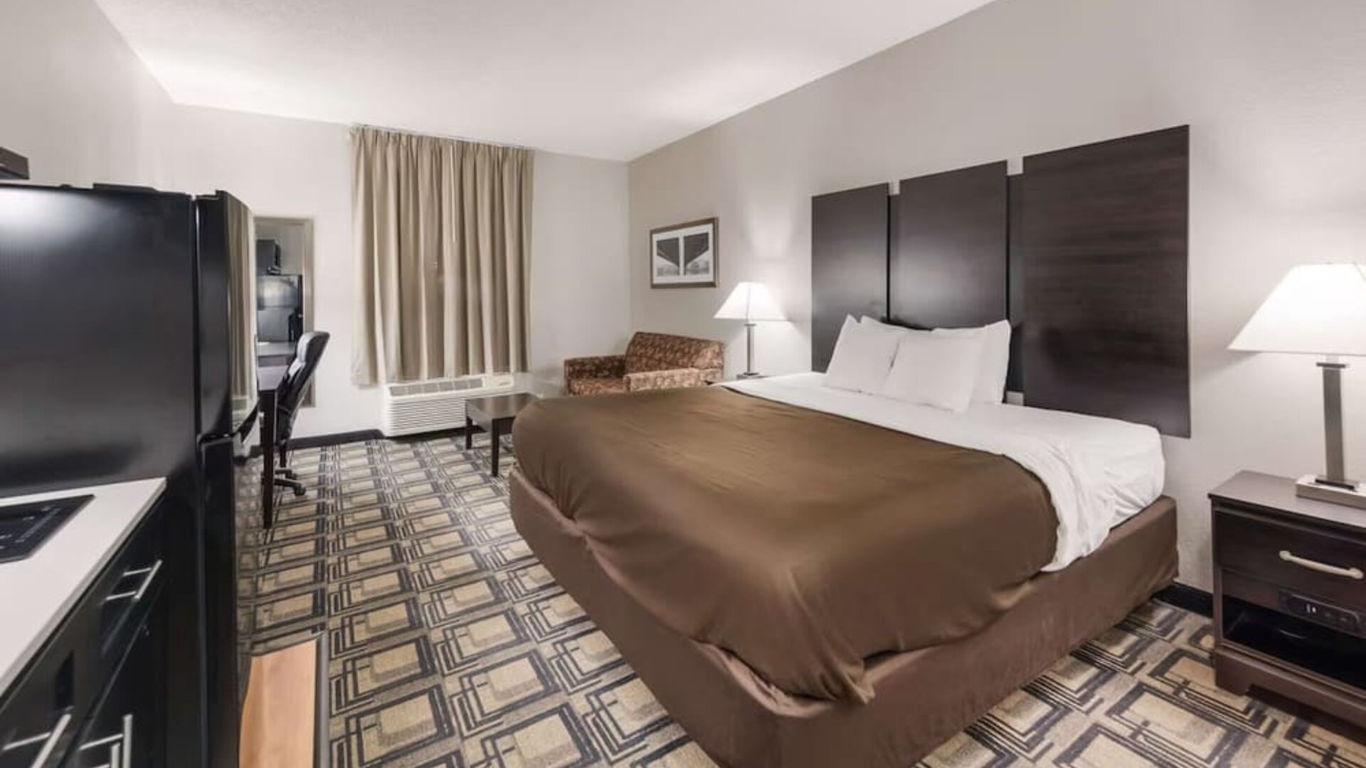 King room with large bed, bedside tables, lamps, and seating area with armchair and table at Suburban Studios Mason Hwy-42.