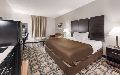 King room with large bed, bedside tables, lamps, and seating area with armchair and table at Suburban Studios Mason Hwy-42.