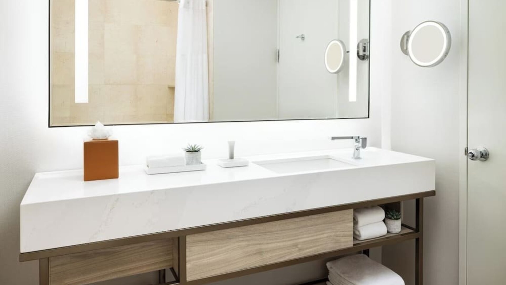 Modern bathroom with large mirror, vanity sink, mounted magnifying mirror, and neatly arranged towels at M Social New York Downtown.