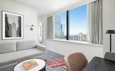 Lounge area with sofa seating, floor lamp, wall art, and large window overlooking city buildings at M Social New York Downtown.