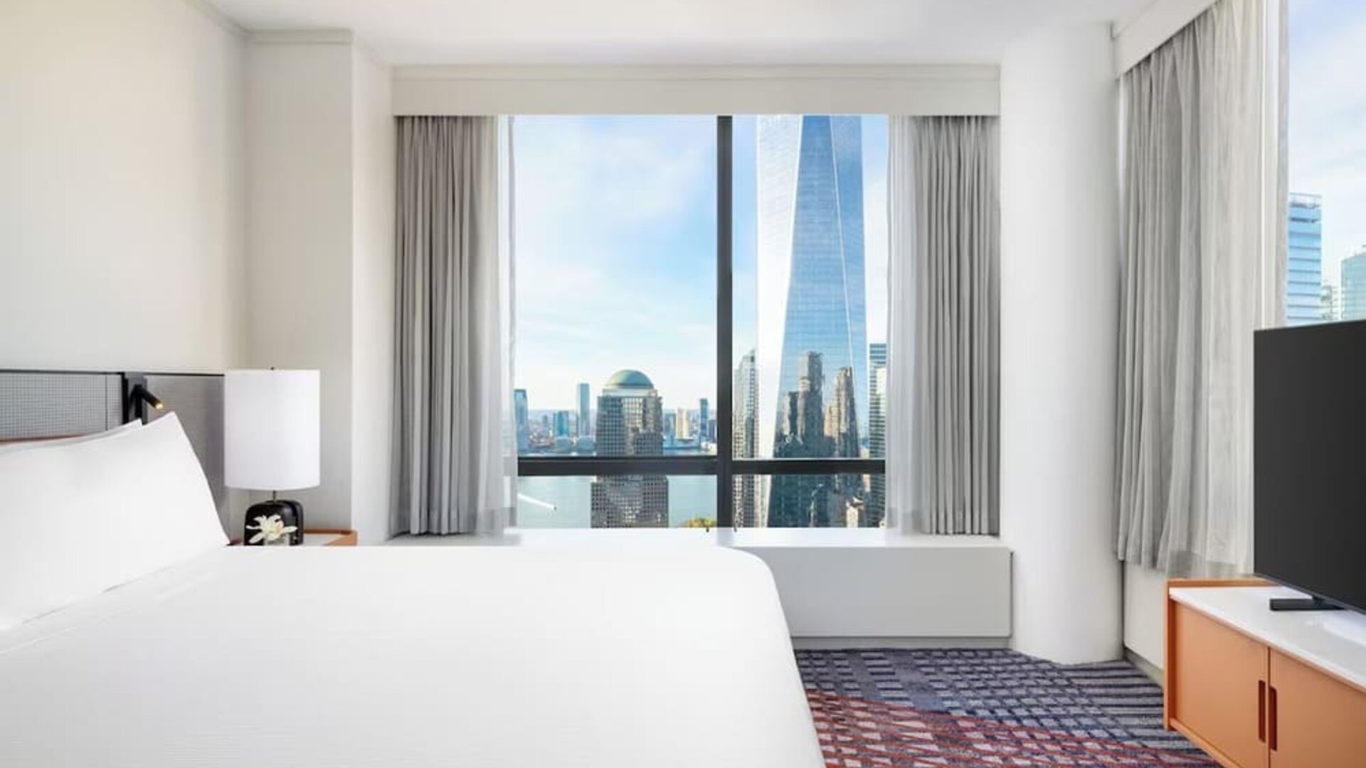 Guest room with king bed, large window, and city skyline view at M Social New York Downtown.