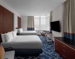 Guest room with two double beds, workspace desk, chair, and large windows at Hilton Brooklyn New York.