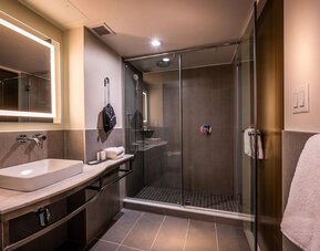 Bathroom with walk-in glass shower, sink, illuminated mirror, and modern finishes at La Quinta Times Square South.