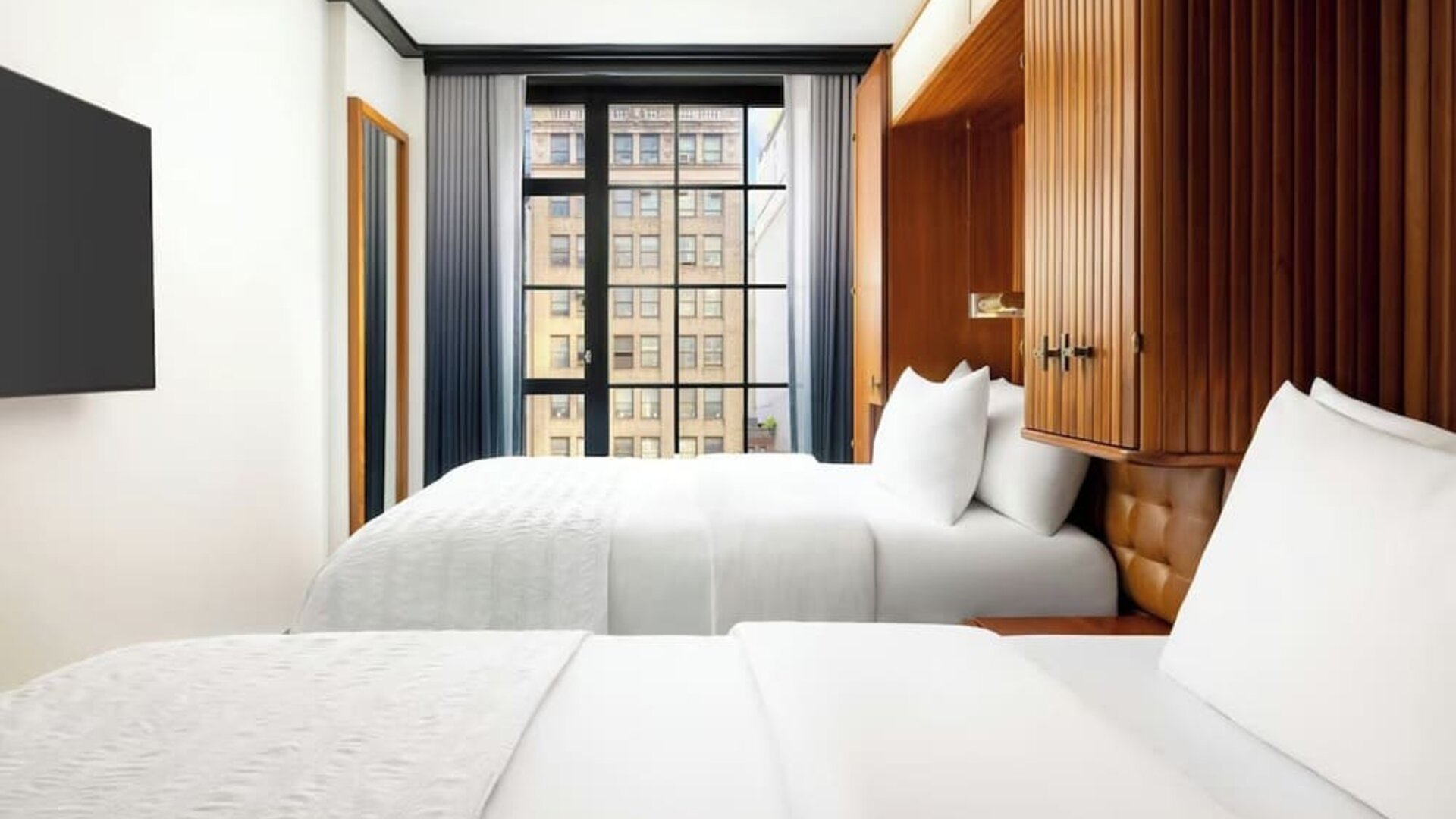 Guest room with two beds, wood-paneled headboard, and large window with city views at Le Méridien New York, Central Park.