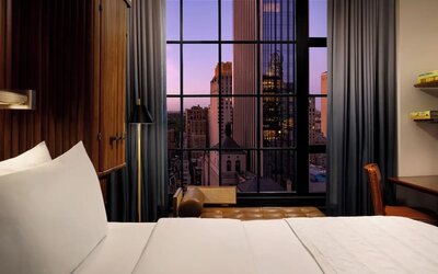 Guest room with king bed and large window showcasing city skyline views at Le Méridien New York, Central Park.