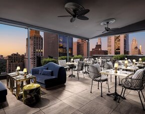 Rooftop terrace with lounge seating, dining tables, and skyline views at Le Méridien New York, Central Park.