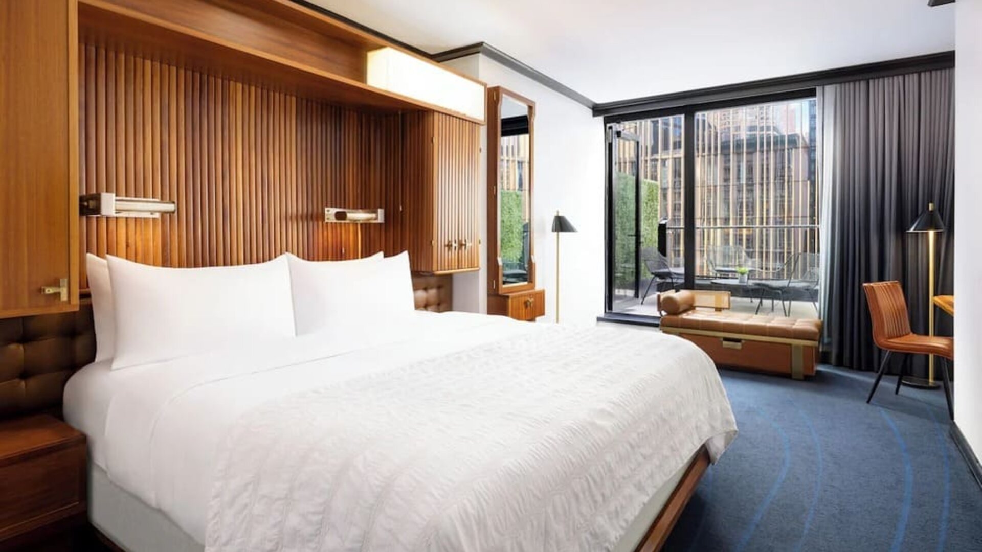 Guest room with king bed, wood accents, and floor-to-ceiling windows with balcony access at Le Méridien New York, Central Park.