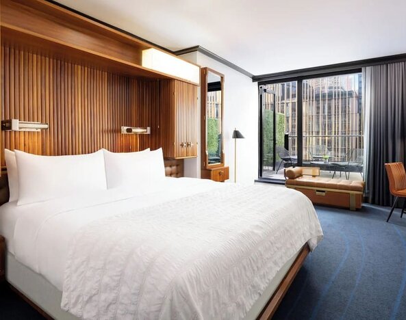 Guest room with king bed, wood accents, and floor-to-ceiling windows with balcony access at Le Méridien New York, Central Park.