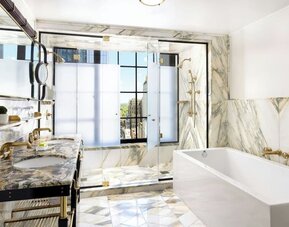 Luxury bathroom with marble finishes, double sink, bathtub, and glass-enclosed shower at Le Méridien New York, Central Park.