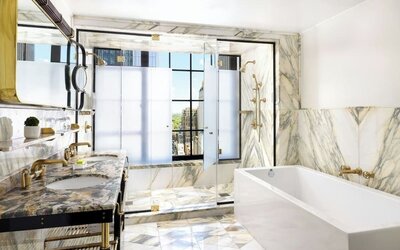 Luxury bathroom with marble finishes, double sink, bathtub, and glass-enclosed shower at Le Méridien New York, Central Park.