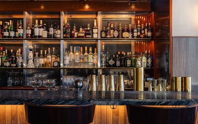 Bar area with shelves of liquor, counter seating, and warm lighting at Le Méridien New York, Central Park.