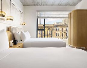 Stylish twin room with two beds, warm lighting, and city-facing window at Timbri Hotel San Francisco, Curio Collection By Hilton.
