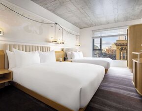 Stylish double room with two beds, warm lighting, contemporary décor, and city-facing window at Timbri Hotel San Francisco, Curio Collection By Hilton.