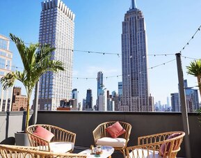 Rooftop terrace with seating, string lights, and skyline views including the Empire State Building at Hotel Hendricks.