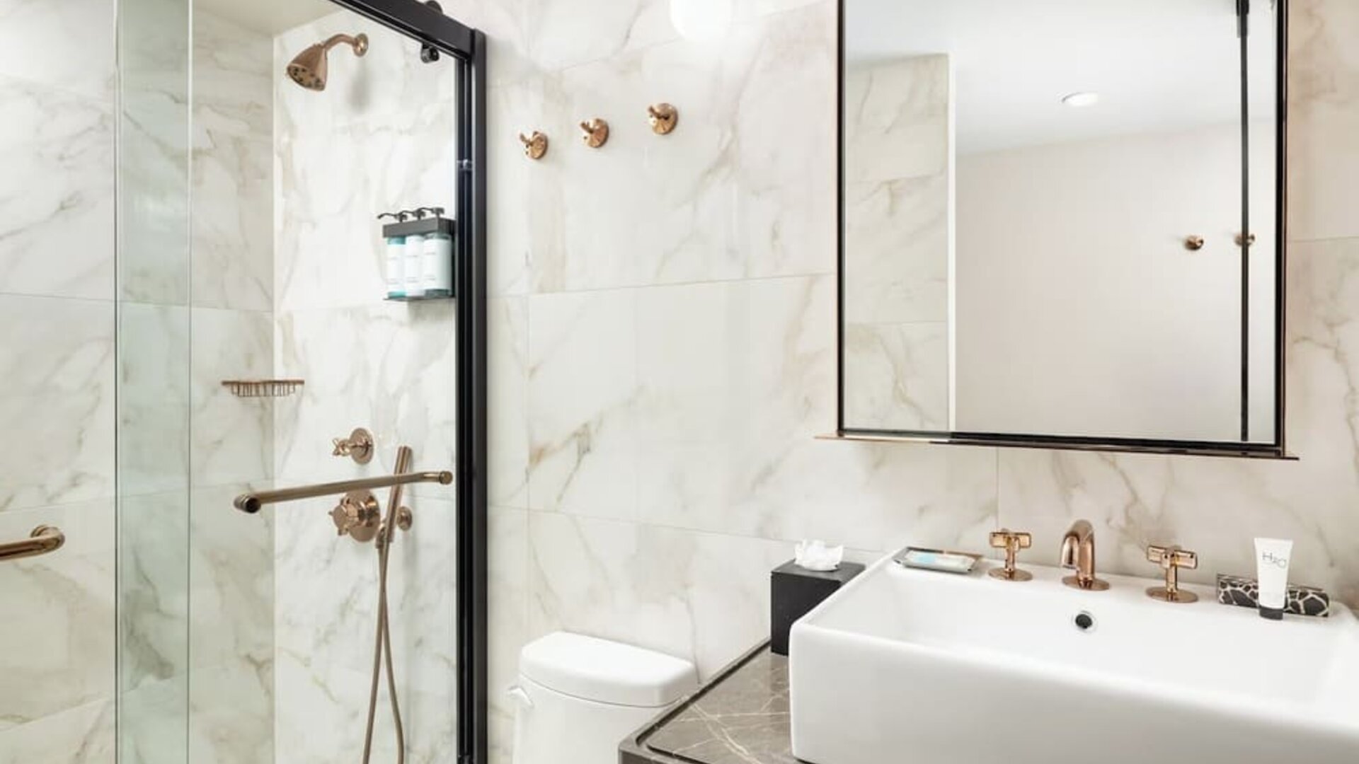 Modern bathroom with walk-in glass shower, marble walls, and sleek vanity with gold fixtures at Hotel Hendricks.