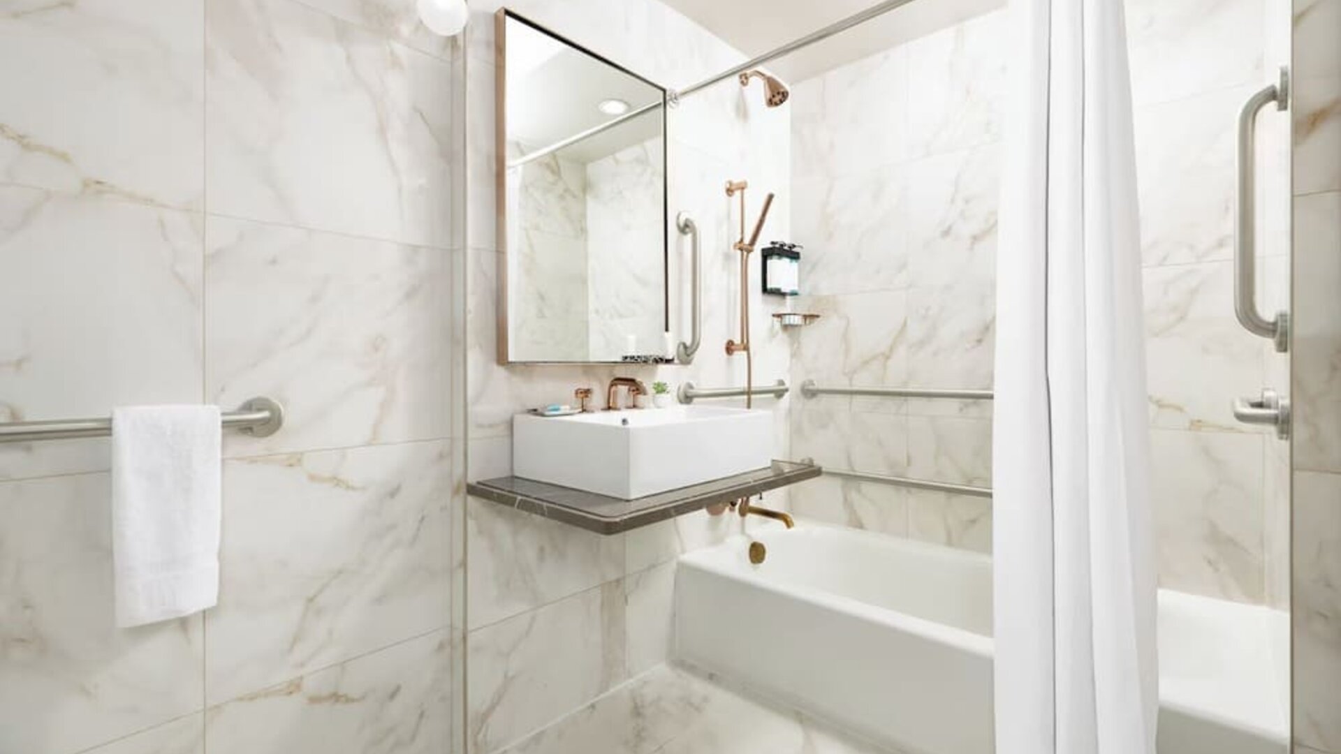 Bathroom with bathtub, marble finishes, grab rails, and contemporary sink area at Hotel Hendricks.