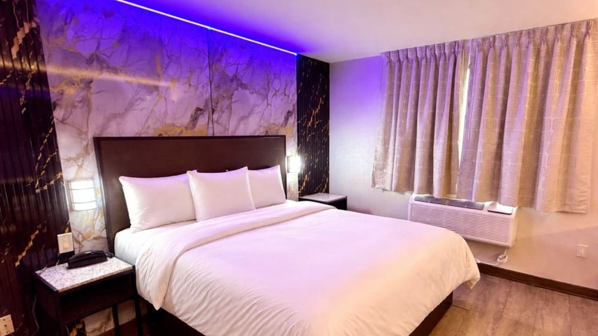 Modern guest room with king bed, marble feature wall, ambient LED lighting, and window with curtains at Imperial Hotel.