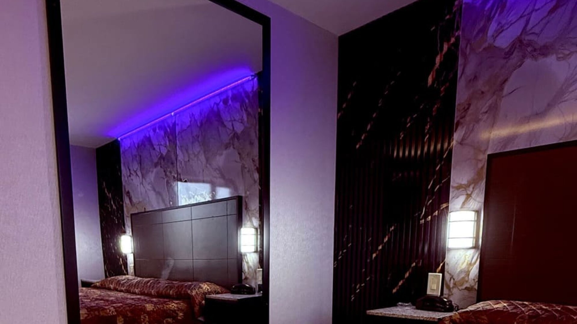 Guest room with large wall mirror, bed with patterned bedding, and accent lighting creating a cozy atmosphere at Imperial Hotel.