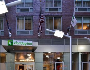 Exterior view of the hotel building façade with signage and flags at Holiday Inn New York City - Times Square By IHG.