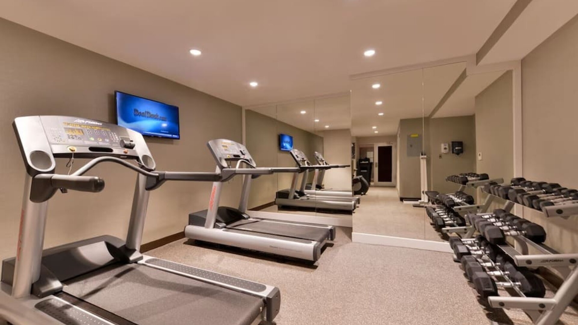Fitness facility with treadmills, free weights, and mirrored walls at Holiday Inn New York City - Times Square By IHG.