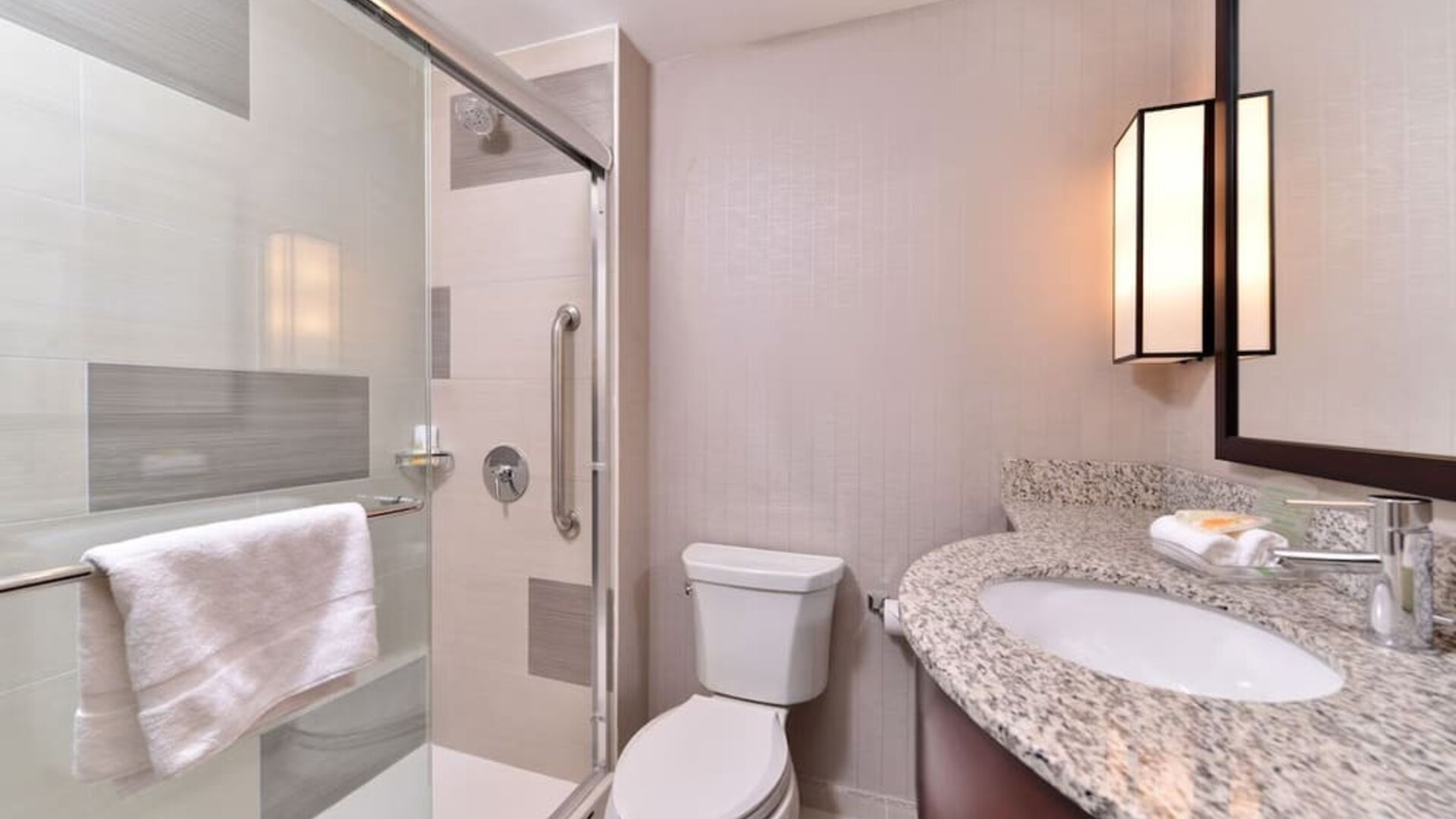 Bathroom with glass-enclosed shower, toilet, vanity sink, and granite countertop at Holiday Inn New York City - Times Square By IHG.