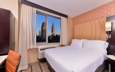 Guest room with king bed and large window showcasing city skyline views at Holiday Inn New York City - Times Square By IHG.