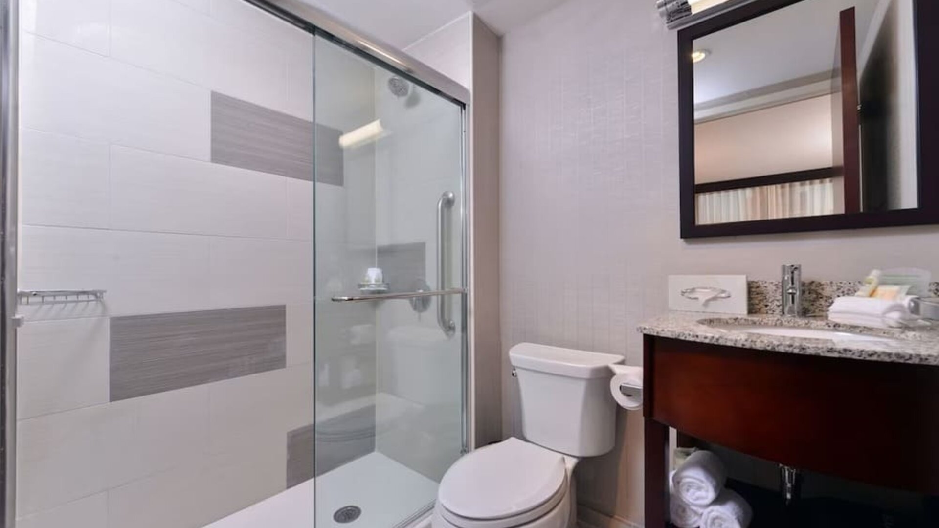 Bathroom with walk-in shower, toilet, curved granite sink, and modern lighting at Holiday Inn New York City - Times Square By IHG.