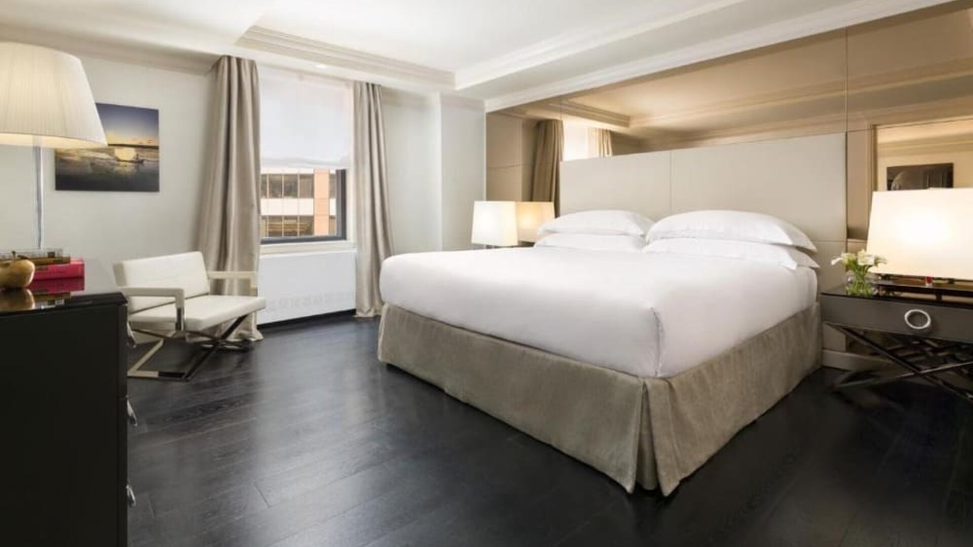 Bright guest room with large windows, neutral tones, and cozy seating at The Michelangelo New York.