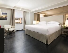 Bright guest room with large windows, neutral tones, and cozy seating at The Michelangelo New York.