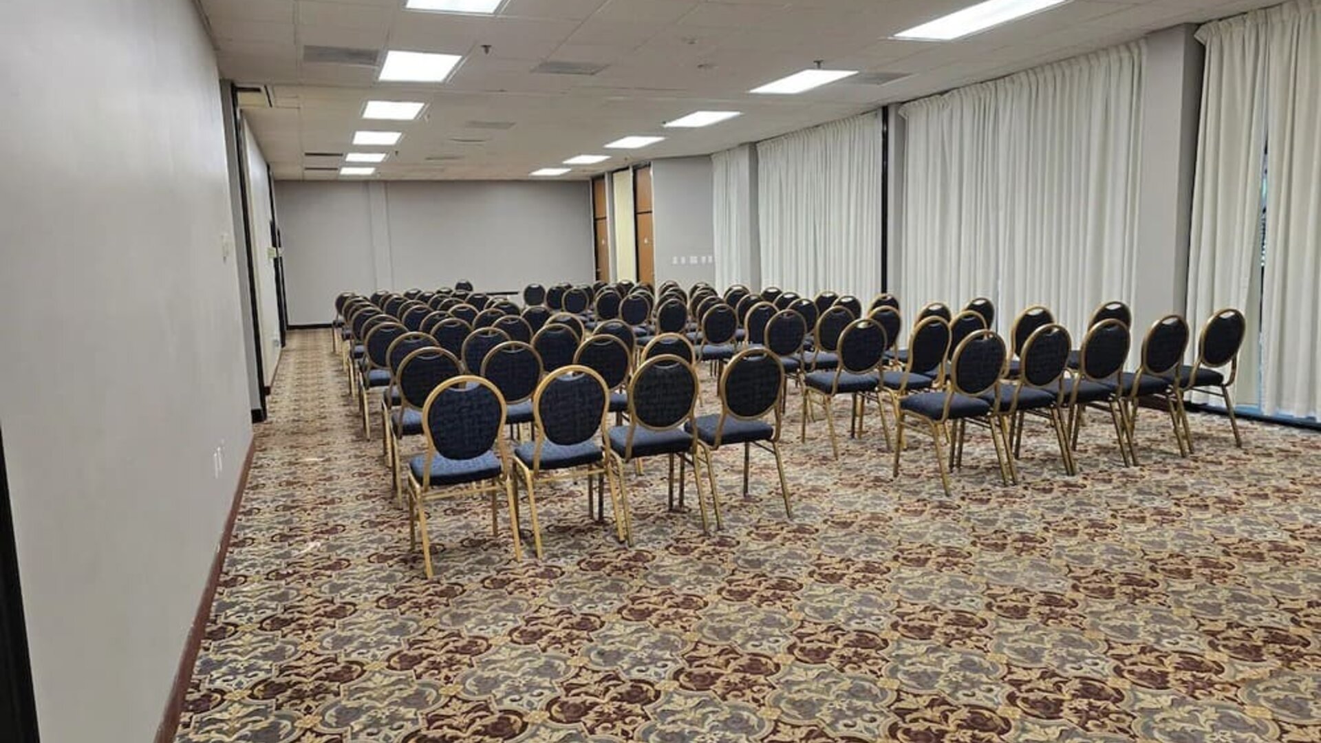 Meeting room with rows of banquet-style chairs, patterned carpet, and bright overhead lighting set up for a conference at Wyndham Garden Williamsburg Busch Gardens Area.