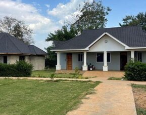 Exterior view of a private lodge unit surrounded by greenery, with a paved walkway and small porch area at Sega Lodge.