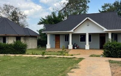 Exterior view of a private lodge unit surrounded by greenery, with a paved walkway and small porch area at Sega Lodge.