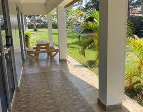 Covered patio area with tiled flooring and picnic-style seating, overlooking the garden at Sega Lodge.
