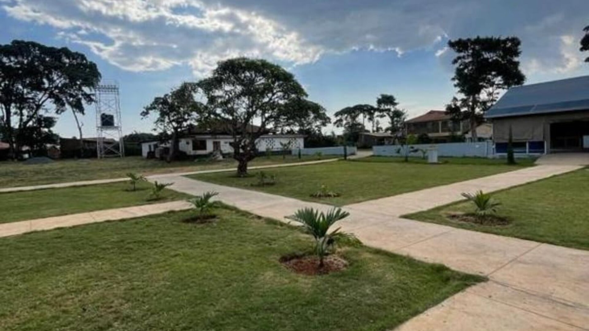 Open outdoor grounds with walking paths, greenery, and scattered lodge buildings under a partly cloudy sky at Sega Lodge.