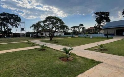 Open outdoor grounds with walking paths, greenery, and scattered lodge buildings under a partly cloudy sky at Sega Lodge.