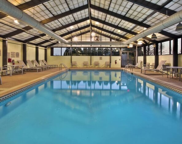 Indoor pool with lounge chairs, skylit ceiling, and large windows along the deck at Marriott SpringHill Suites Naperville/Warrenville.