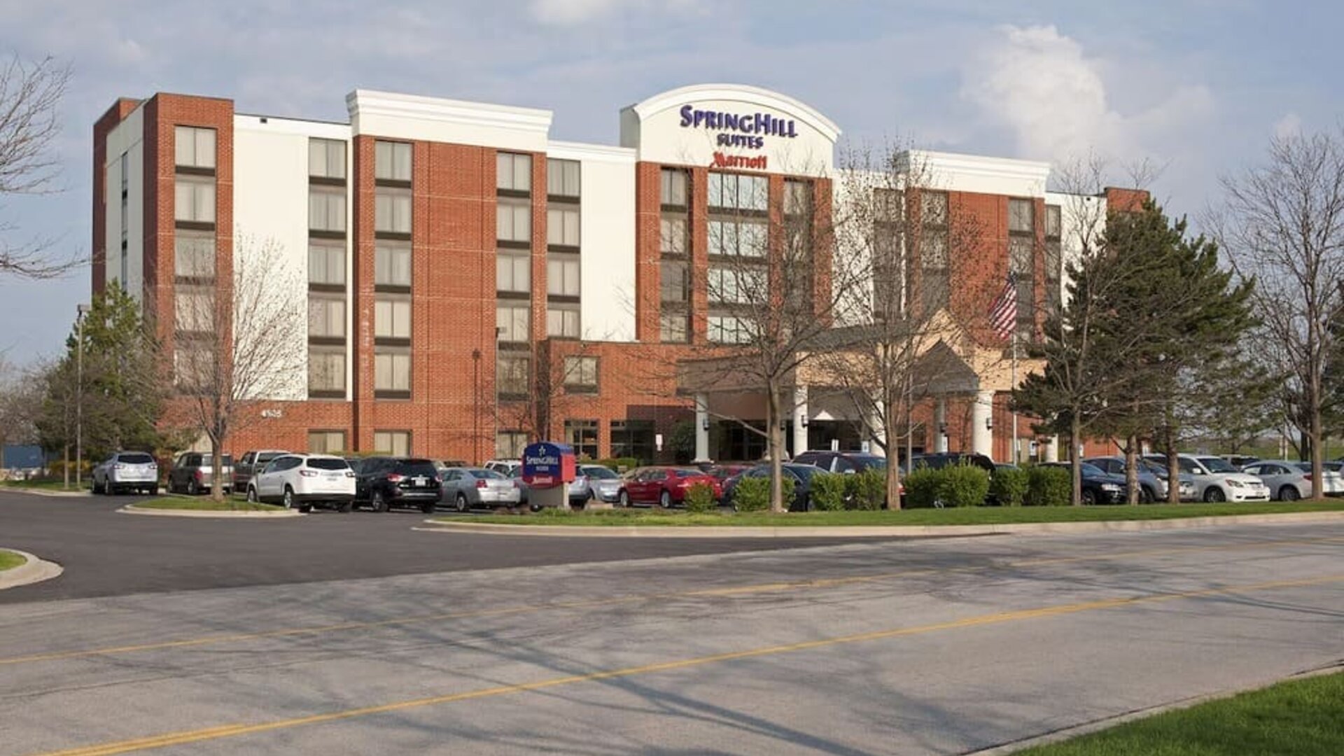 Exterior view of Marriott SpringHill Suites Naperville/Warrenville with red brick facade, covered entrance, and parked cars.
